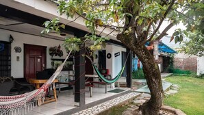Un espacio de descanso al aire libre con techo, una hamaca, un árbol y un patio con baldosas.