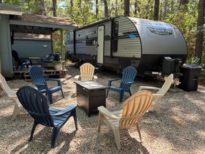 A recreational vehicle (RV) with a kitchen area, surrounded by outdoor seating with Adirondack chairs.