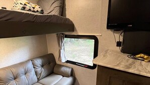 Een compact RV-interieur met een bank, een raam, een televisie en een kast.