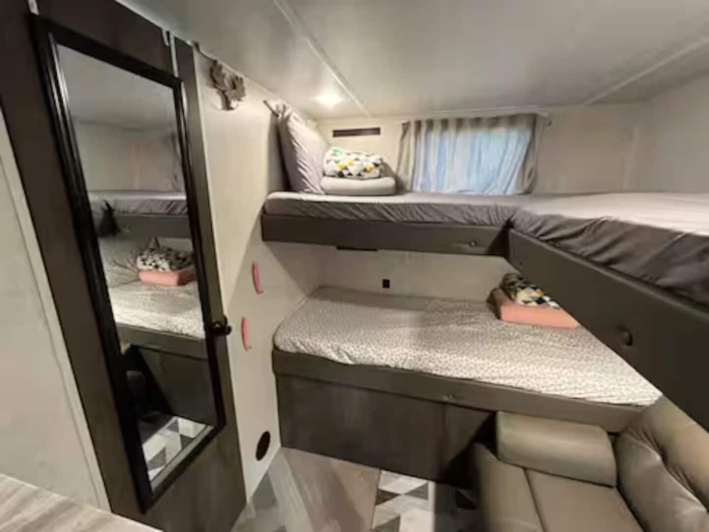 Habitación compacta y bien iluminada con una cama litera, un espacio de descanso pequeño y un espejo.