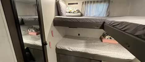 Habitación compacta y bien iluminada con una cama litera, un espacio de descanso pequeño y un espejo.