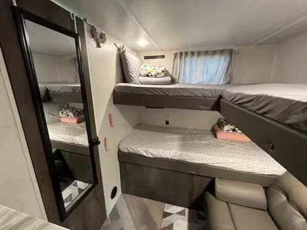 A compact, well-lit room with a bunk bed, a small seating area, and a mirror.