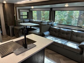 A modern RV interior with a kitchenette, seating area, and large windows.