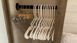 Een houten kast met een kledingstang en meerdere metalen ophanghaakjes.