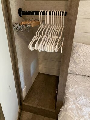 Um armário de madeira com barra para pendurar roupas e vários cabides de metal.