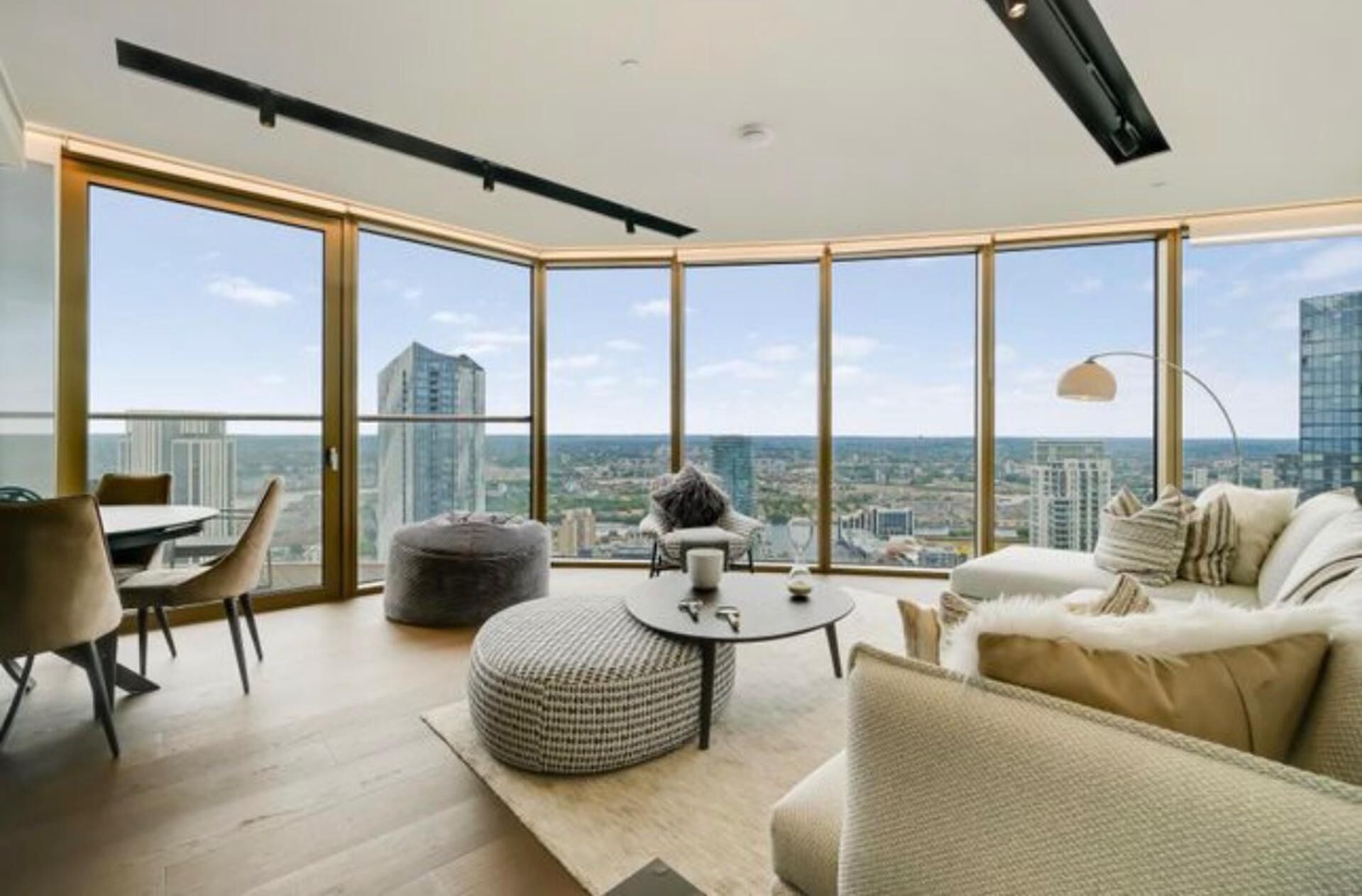 Un salon moderne offrant une vue panoramique sur la ville, avec un pouf rond, un canapé et une table à manger.