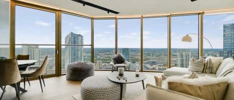 A modern living room with a panoramic city view, a round ottoman, a sofa, and a dining table.