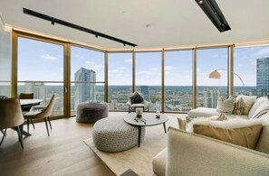 A modern living room with a panoramic city view, a round ottoman, a sofa, and a dining table. - Luxury London Apartment With 3 Bedrooms (London)
