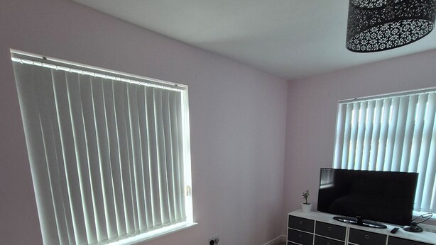 Un dormitorio con cama, televisor sobre un mueble y ventana con persianas.