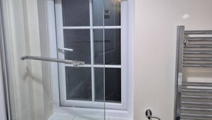 Un baño con cabina de ducha de vidrio, una ventana blanca con panel de vidrio esmerilado y un perchero de metal.