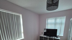 Un dormitorio con una cama, un televisor sobre una cómoda y una bolsa de compras.