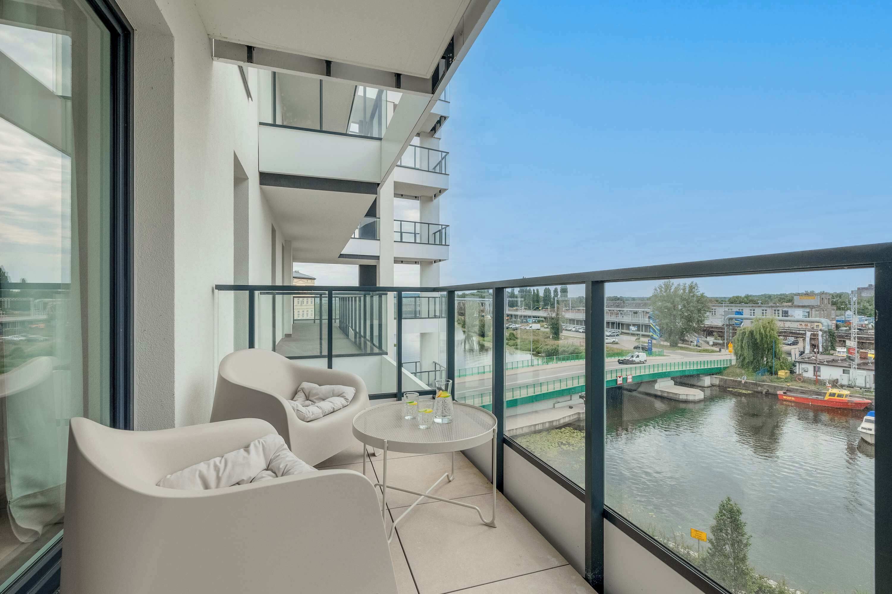 A balcony with a view of a river, a table with glasses, and two chairs.