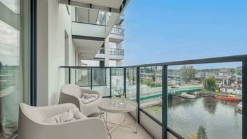 A balcony with a view of a river, a table with glasses, and two chairs.
