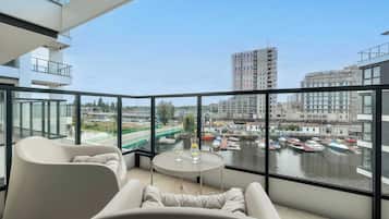 A modern balcony with a view of a river and boats, a glass railing, and a seating area with a table.