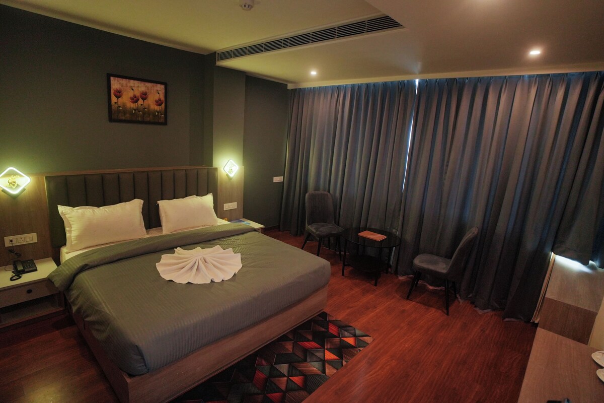 A hotel room with a bed, bedside tables, a chair, a small table, and a window with curtains.