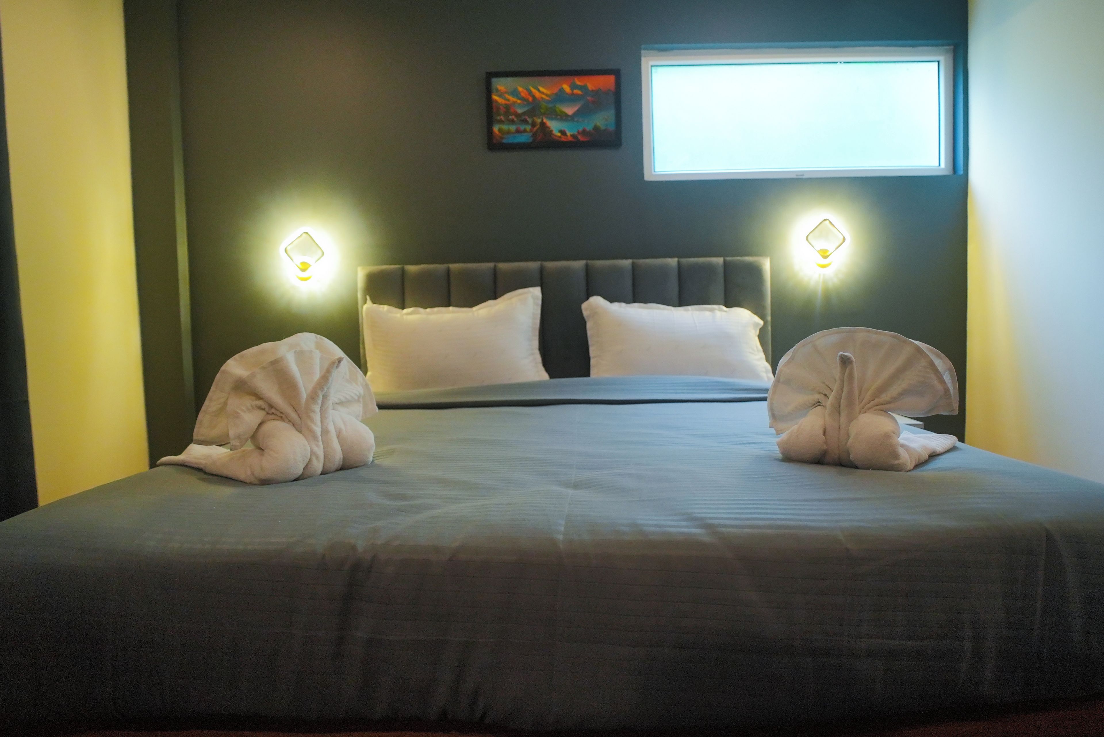A neatly made bed with pillows, a headboard, and two wall-mounted light fixtures.
