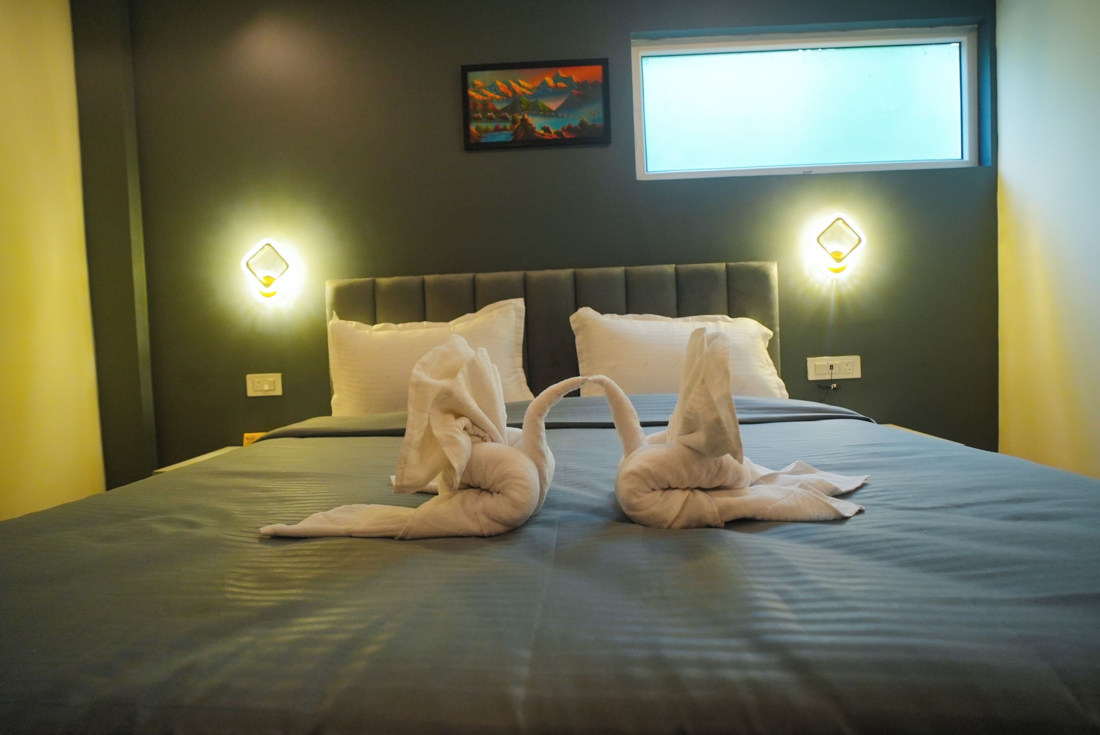 A hotel room with a bed, two wall-mounted light fixtures, and a painting on the wall.