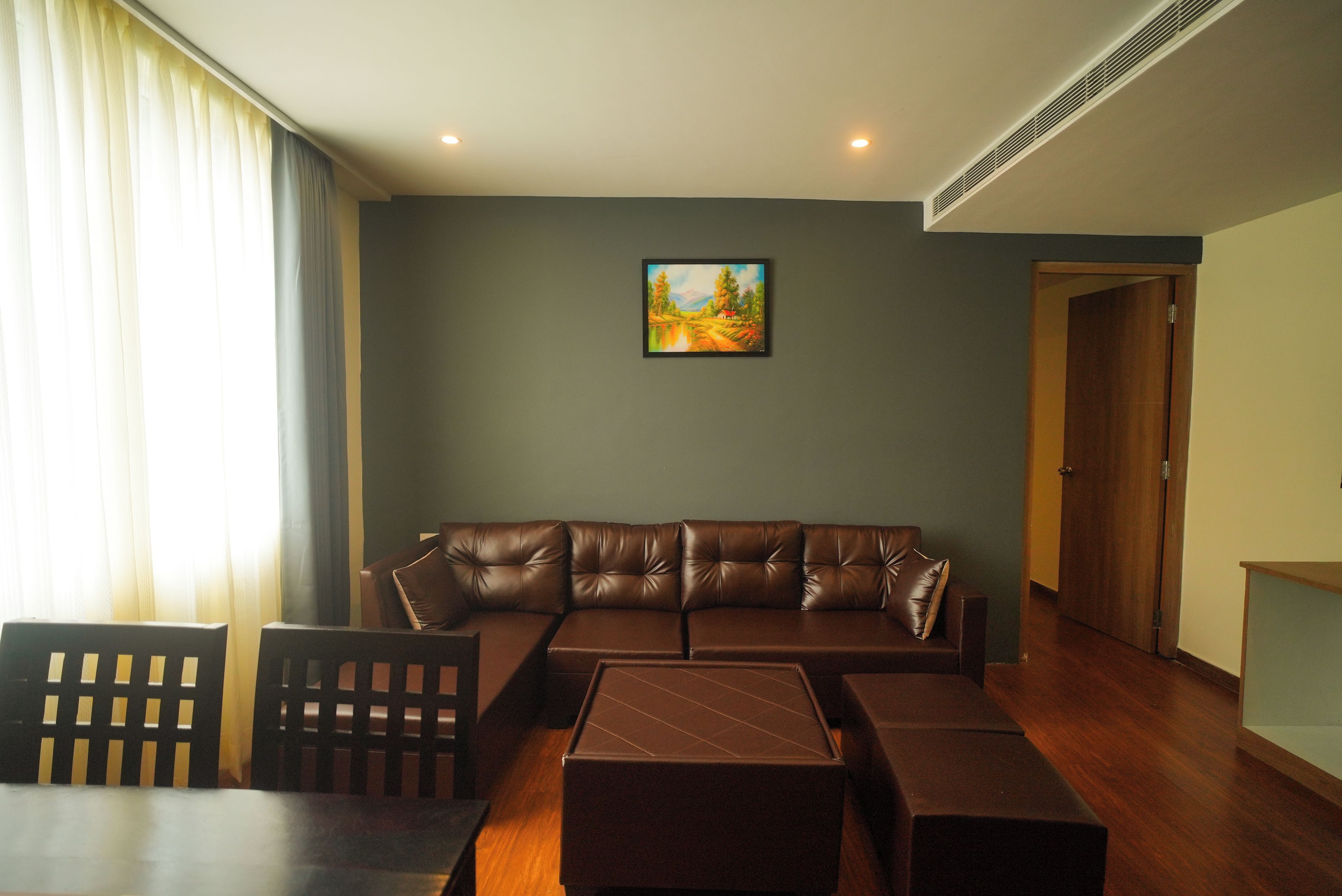 A living room with a brown leather sofa, a painting on the wall, and a wooden door.