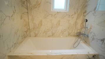 A bathroom with a marble wall, a bathtub, and a shower area.