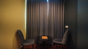 A small room with two chairs and a table, a curtain, and a light switch on the wall. - Meraki Hotels & Resorts Sikkim (Gangtok)