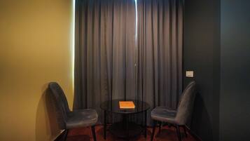 Una habitación pequeña con dos sillas, una mesa, una cortina y un interruptor de luz en la pared.
