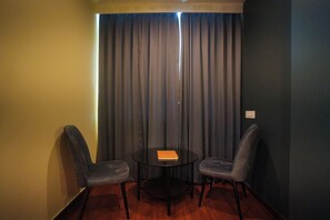 Quarto pequeno com duas cadeiras, uma mesa, cortina e interruptor na parede.