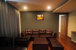 A living room with a sectional sofa, a coffee table, and a painting on the wall. - Meraki Hotels & Resorts Sikkim (Gangtok)