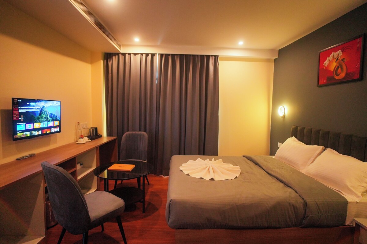 A hotel room with a bed, a desk, a chair, a television, and a painting on the wall.