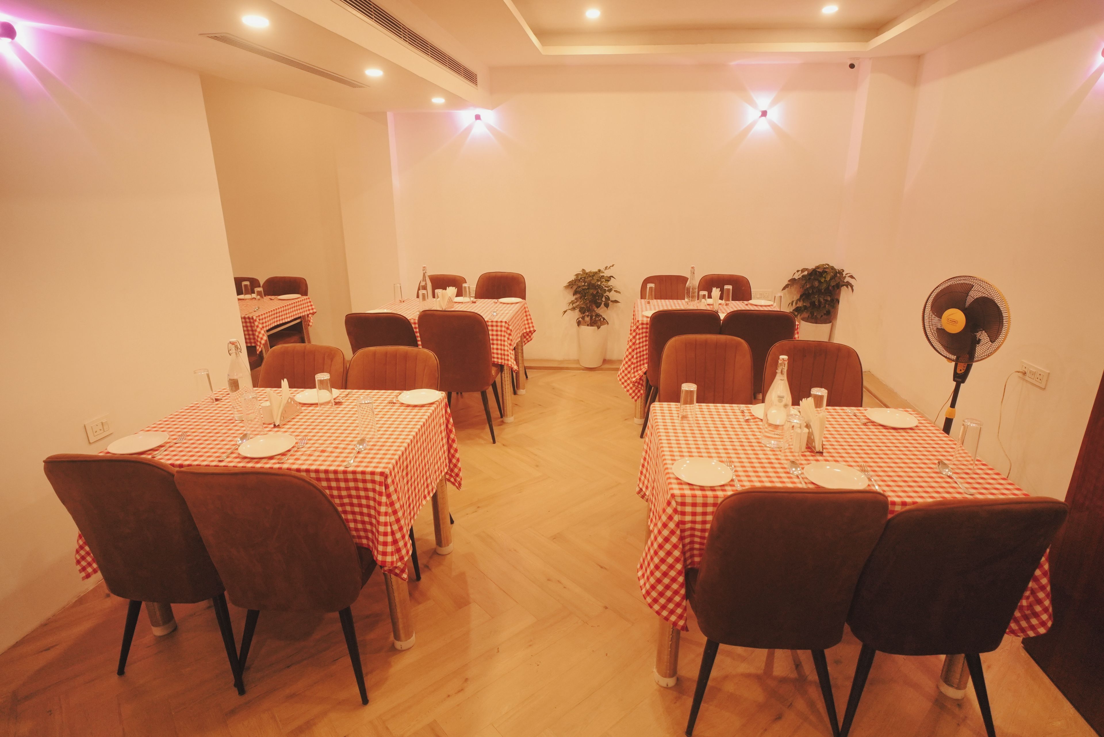 Un comedor con varias mesas dispuestas para comidas, sillas y un ventilador.