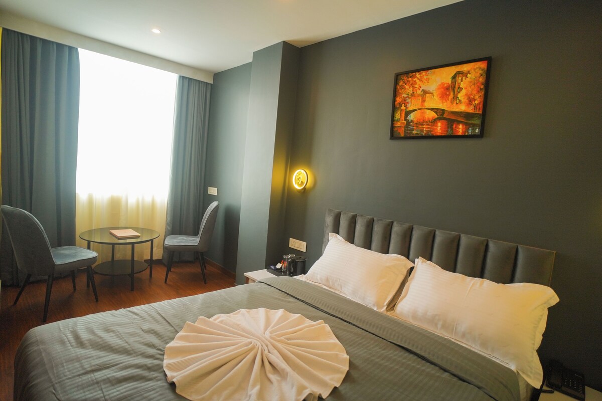 A hotel room with a bed, a desk, a chair, and a painting on the wall.
