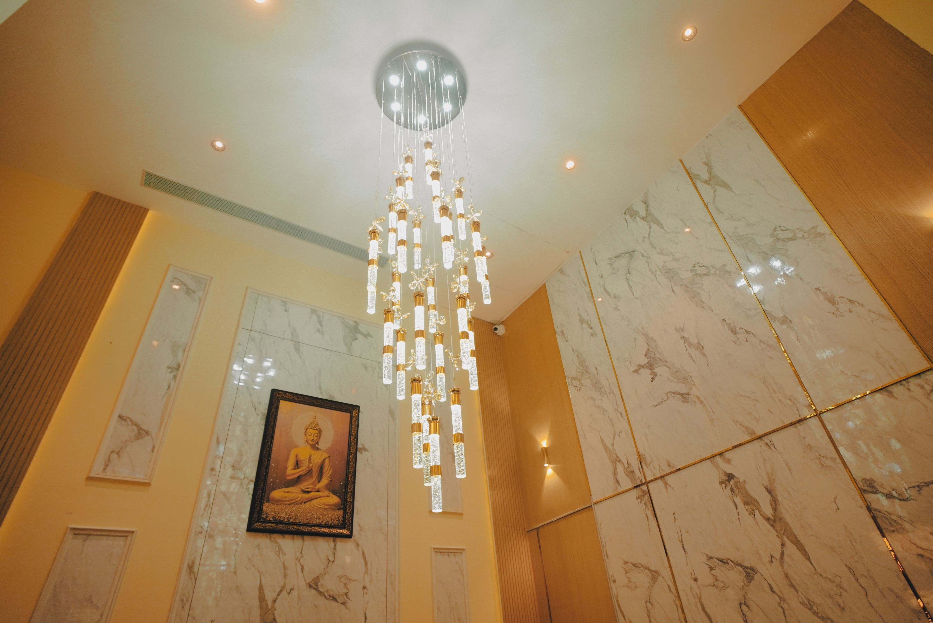 A room with a hanging chandelier, marble walls, and a Buddha statue.