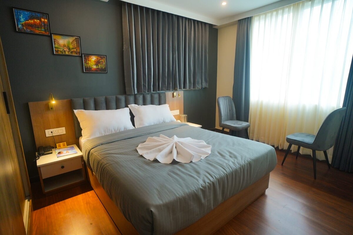 Habitación de hotel con una cama grande, una mesita de noche con lámpara, una silla y una obra de arte en la pared.