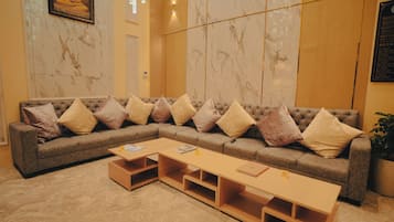 Un moderno vestíbulo de hotel con un amplio sofá modular, una mesa de centro de madera y paredes de mármol.