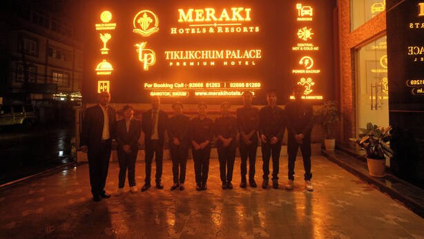 A group of people standing in front of a hotel entrance with illuminated signage indicating amenities such as a multi cuisine restaurant, bar, banquet, and parking. - Meraki Hotels & Resorts Sikkim (Gangtok)