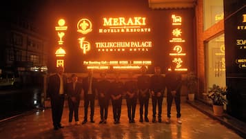 Un grupo de personas frente a la entrada de un hotel, con señalización iluminada que indica servicios como restaurante con cocina internacional, bar, salón de banquetes y estacionamiento.
