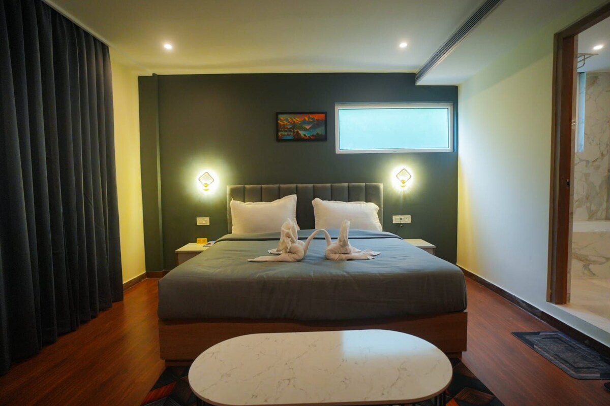 Una habitación de hotel con cama, mesitas de noche, una mesa redonda y un cuadro en la pared.