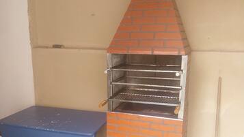 A brick-built outdoor grill with multiple shelves and a table nearby.