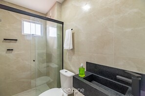Uma casa de banho moderna com cabine de chuveiro em vidro, sanita e lavatório com bancada preta.