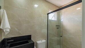 Un bagno moderno con box doccia in vetro, lavandino nero e asciugamano bianco appeso al muro.