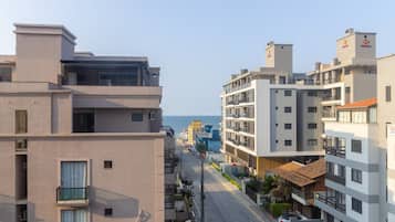 A modern urban street with multi-story buildings, a clear sky, and a view of the sea.