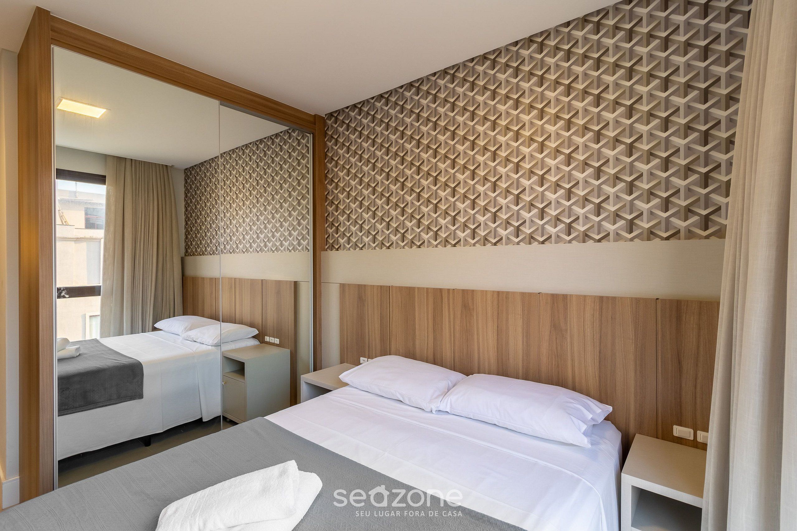 A hotel room with two beds, a large mirror, and a patterned wall.