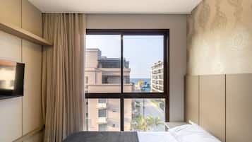A hotel room with a bed, a TV, a large window with a view of buildings and a street, and a patterned wall.