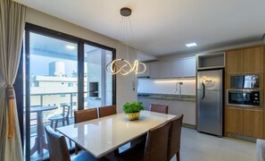 A modern kitchen with stainless steel appliances, a dining area with a table and chairs, and large windows offering a view of the cityscape. - Apt sea View, Pool Condo, 300m to Beach Csd0302 (Bombinhas)