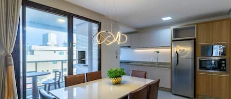 A modern kitchen with stainless steel appliances, a dining area with a table and chairs, and large windows offering a view of the cityscape.