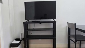 A black TV stand with a flat-screen TV on top, a white trash bin, and a wooden floor. - Cosy Flat near Canary Wharf | Sleeps 6 (London)