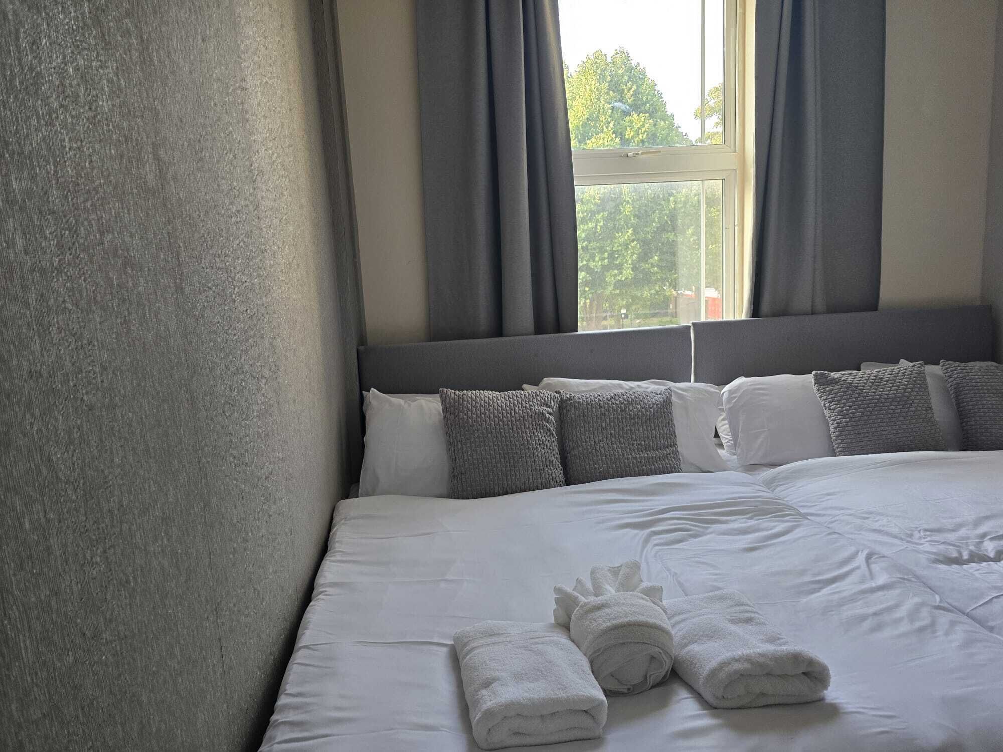 Une chambre d’hôtel avec un grand lit, des rideaux gris et une vue sur les arbres par la fenêtre.