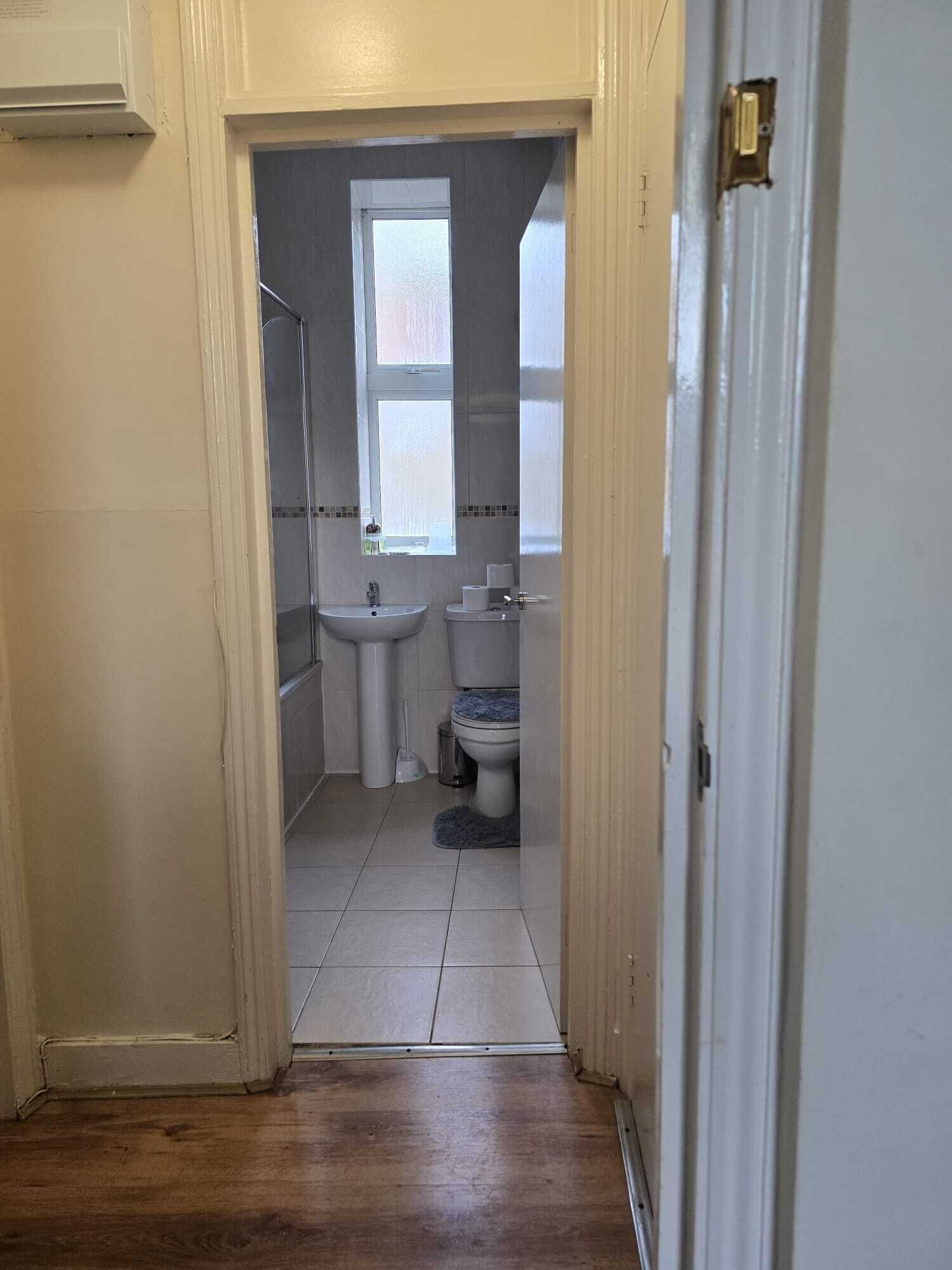 A narrow hallway leading to a bathroom with a toilet, sink, and window.
