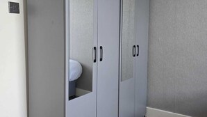 A grey wardrobe with two doors and a small window, located in a room with wooden flooring and a grey textured wall. - Cosy Flat near Canary Wharf | Sleeps 6 (London)