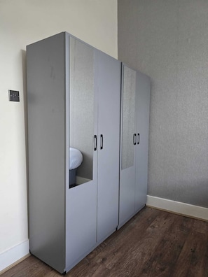 A grey wardrobe with two doors and a small window, located in a room with wooden flooring and a grey textured wall. - Cosy Flat near Canary Wharf | Sleeps 6 (London)