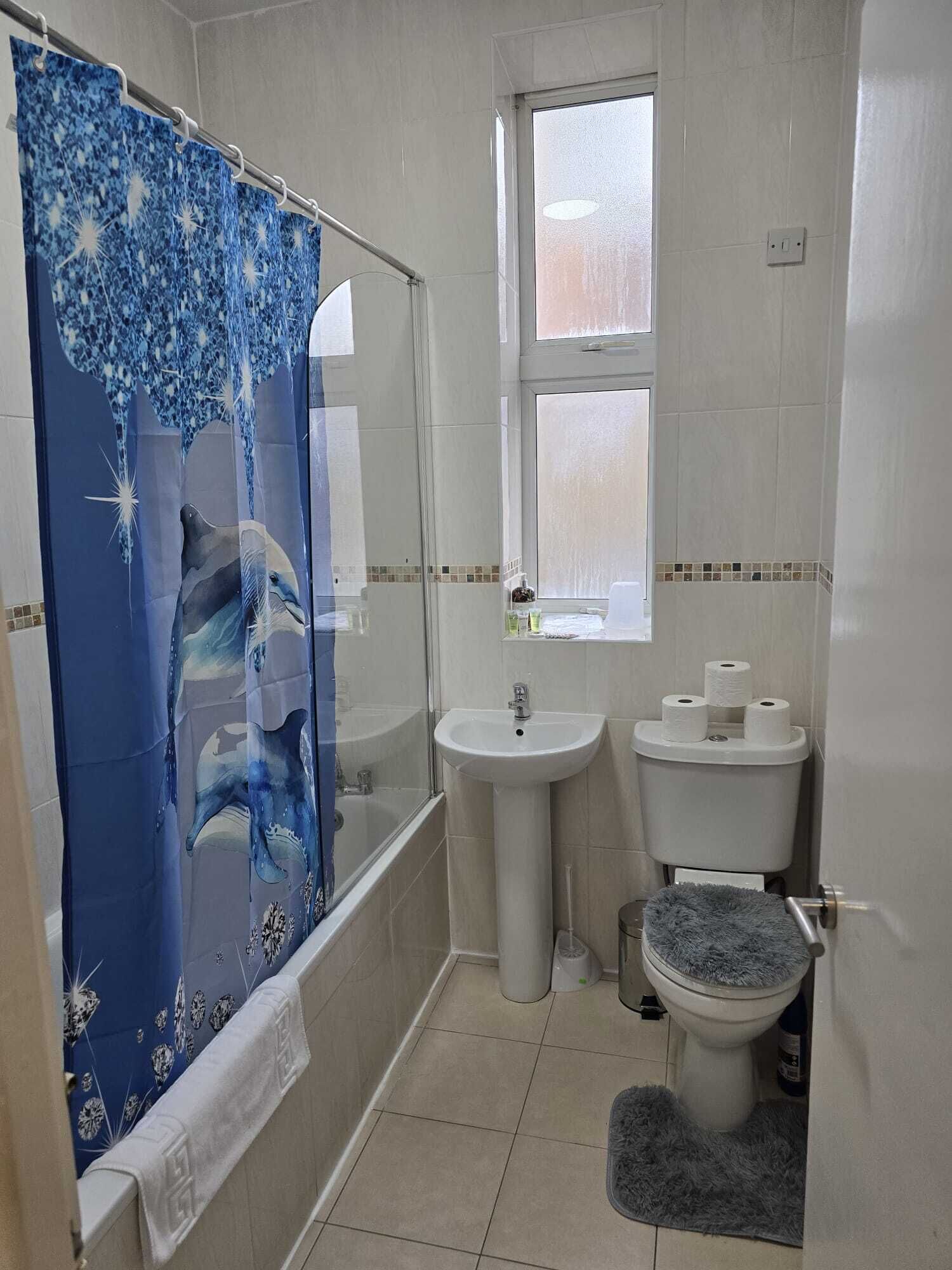 A bathroom with a shower, sink, toilet, and a window.